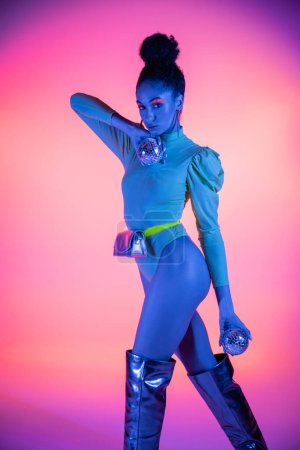 Trendiges afrikanisch-amerikanisches Model mit Neon-Make-up, das Discokugeln auf rosa Hintergrund hält