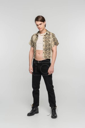 full length of bigender person in animal print blouse and black pants standing on grey background