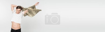Téléchargez les photos : Joyeux modèle bigender en t-shirt blanc imprimé peau de serpent isolé sur gris, bannière - en image libre de droit