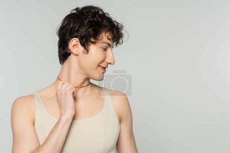 profile of curly bigender model in tank top touching colorful beads isolated on grey