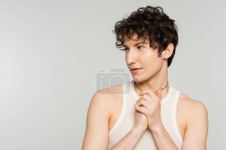young brunette bigender model with wavy hair and nose piercing looking away isolated on grey