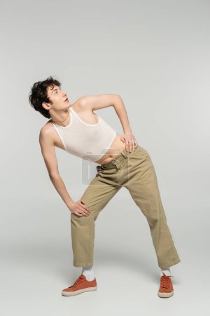 Photo for Full length of trendy pansexual person in crop top and beige pants looking away on grey background - Royalty Free Image