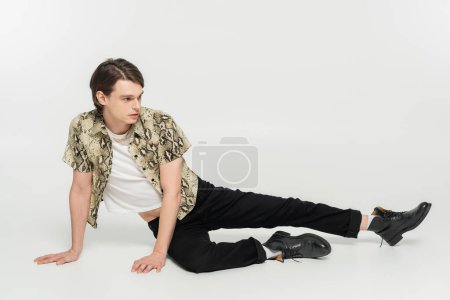 Téléchargez les photos : Longueur totale de la personne pansexuel élégant en peau de serpent imprimé chemisier et pantalon noir posant sur fond gris - en image libre de droit