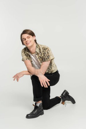 Photo for Full length of cheerful nonbinary model in black pants and animal print blouse looking away on grey background - Royalty Free Image