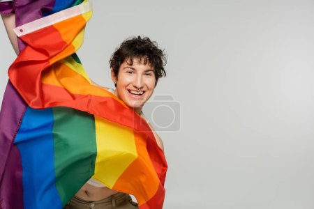 overjoyed pangender model with lgbt flag looking at camera isolated on grey