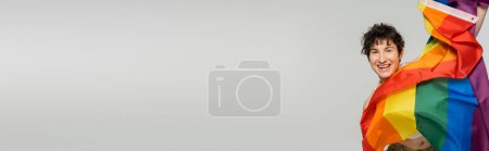Photo for Excited pansexual person wrapped in lgbt flag smiling at camera isolated on grey, banner - Royalty Free Image