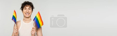 Photo for Cheerful bigender person in tank top holding small lgbt flags isolated on grey, banner - Royalty Free Image