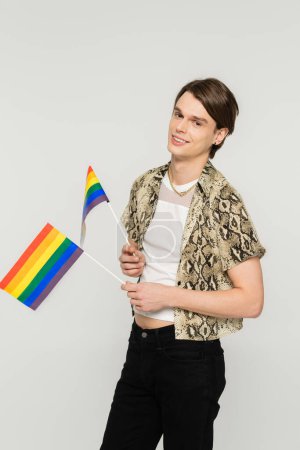 Photo for Happy bigender person in snakeskin print blouse holding small lgbt flags isolated on grey - Royalty Free Image