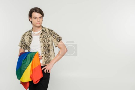 stylish pansexual model with lgbt flag standing with hand on hip and looking at camera isolated on grey