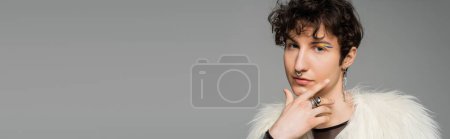 Photo for Portrait of brunette pansexual model in white faux fur jacket and silver accessories isolated on grey, banner - Royalty Free Image