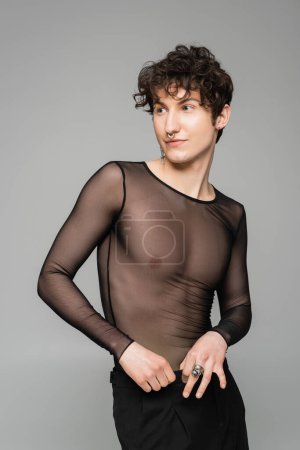 brunette nonbinary model in black transparent top looking away isolated on grey