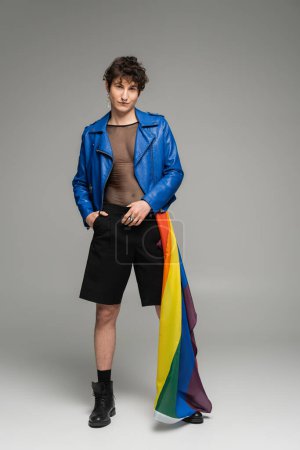Foto de Longitud completa de la persona pansexual con bandera lgbt posando en chaqueta de cuero azul y pantalones cortos negros sobre fondo gris - Imagen libre de derechos