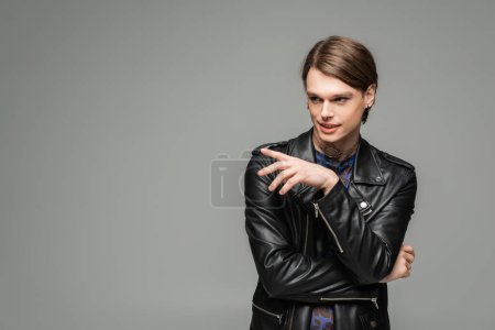 Foto de Persona grande de moda en chaqueta de cuero negro sonriendo y señalando con el dedo aislado en gris - Imagen libre de derechos