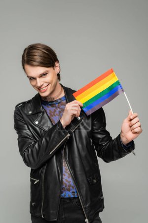 Téléchargez les photos : Heureux pansexuel personne en cuir noir veste tenant petit drapeau lgbt isolé sur gris - en image libre de droit