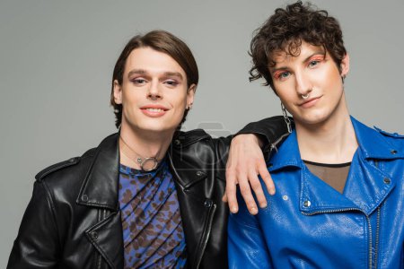 carefree pansexual partners in leather jackets and makeup looking at camera isolated on grey