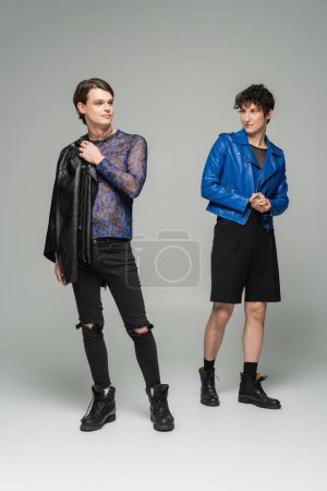 full length of fashionable nonbinary couple standing on grey background