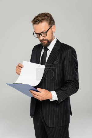 homme d'affaires bien habillé dans des lunettes tenant le presse-papiers et le papier isolé sur gris 