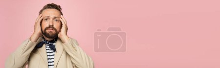 Téléchargez les photos : Homme tendu en blazer et foulard de cou regardant la caméra tout en tenant la tête isolée sur rose, bannière - en image libre de droit