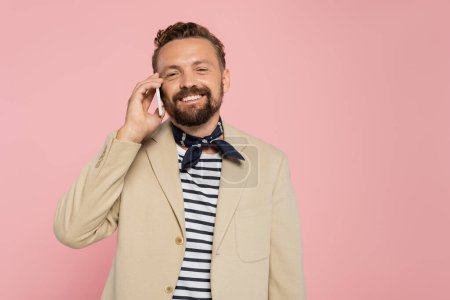 glücklicher französischer Mann in Blazer und Halstuch spricht auf Smartphone isoliert auf rosa 