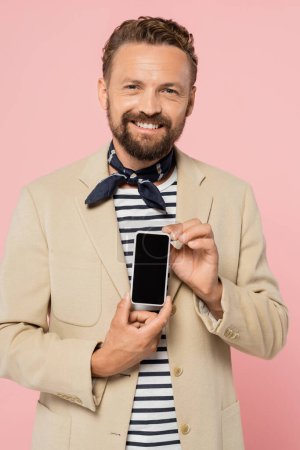 hombre francés lleno de alegría en chaqueta y cuello bufanda celebración de teléfono inteligente con pantalla en blanco aislado en rosa 