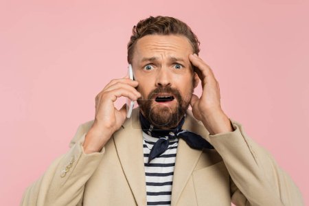 shocked french man in blazer and neck scarf talking on smartphone isolated on pink 