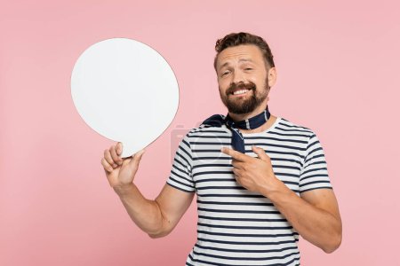 happy french man in striped t-shirt and neck scarf pointing at blank speech bubble isolated on pink 