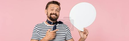 happy french guy in striped t-shirt and neck scarf holding speech bubble isolated on pink, banner 