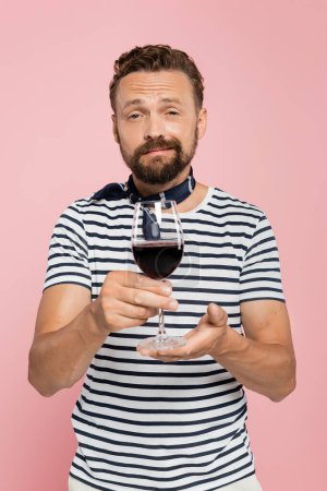 bearded french man in striped t-shirt holding glass of red wine isolated on pink 