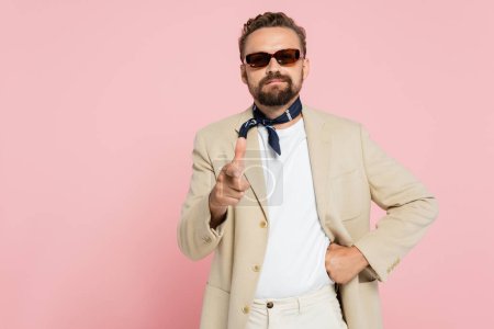 Téléchargez les photos : Élégant français gars dans le cou écharpe et lunettes de soleil pointant vers la caméra isolé sur rose - en image libre de droit