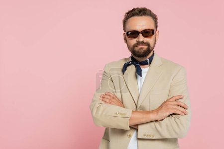 Téléchargez les photos : Élégant français dans le cou écharpe et lunettes de soleil debout avec les bras croisés isolé sur rose - en image libre de droit