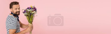 Téléchargez les photos : Homme français souriant en t-shirt rayé et foulard tenant des fleurs sauvages isolées sur rose, bannière - en image libre de droit
