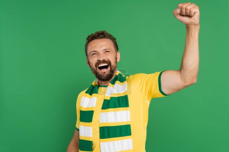 Emotionaler Sportfan in gestreiftem Schal und gelbem T-Shirt jubelt vereinzelt auf Grün 