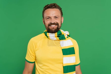 Foto de Ventilador deportivo positivo en bufanda a rayas y camiseta amarilla mirando a la cámara aislada en verde - Imagen libre de derechos