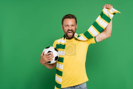 Téléchargez les photos : Ventilateur de football excité en écharpe rayée tenant le football isolé sur vert - en image libre de droit