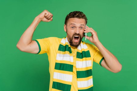 emotional man in striped scarf screaming while talking on mobile phone isolated on green Poster 649955662