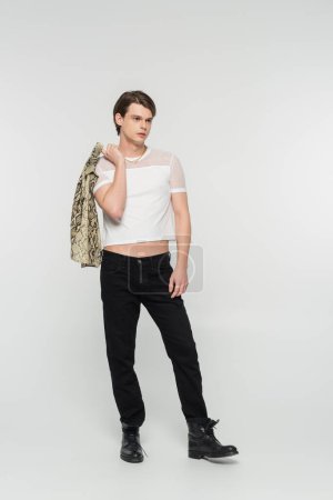 full length of bigender person in trendy clothes holding snakeskin print blouse on grey background