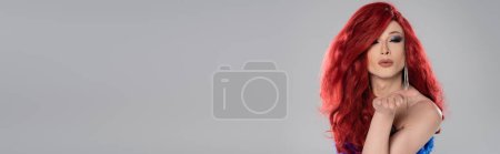 Drag queen in red wig blowing air kiss at camera isolated on grey, banner 