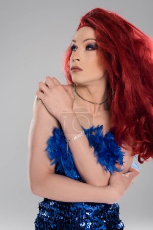 Foto de Persona transgénero en peluca roja y vestido tocando brazo aislado en gris - Imagen libre de derechos