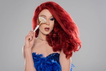 Téléchargez les photos : Drag queen élégant en perruque tenant brosse de maquillage près du visage isolé sur gris - en image libre de droit