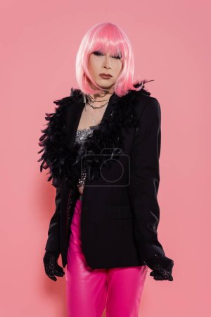 Portrait of drag queen in gloves and jacket looking at camera on pink background 