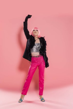 Foto de Longitud completa de drag queen con estilo en la chaqueta con plumas posando sobre fondo rosa - Imagen libre de derechos