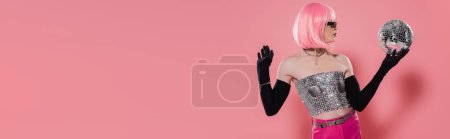 Foto de Vista lateral de la elegante drag queen en la parte superior brillante y guantes que sostienen la bola disco sobre fondo rosa, pancarta - Imagen libre de derechos