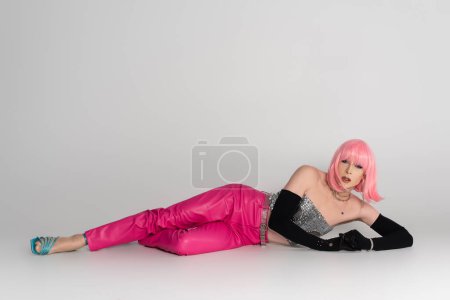 Foto de Elegante drag queen en guantes y la parte superior mirando a la cámara mientras está acostado sobre fondo gris - Imagen libre de derechos