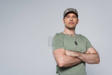 military man in t-shirt and cap standing with folded arms during memorial day isolated on grey 