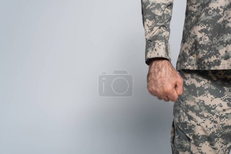 Foto de Vista recortada del soldado patriótico en uniforme militar de pie con el puño cerrado sobre fondo gris - Imagen libre de derechos