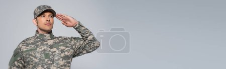 Soldat américain en uniforme militaire avec casquette saluant pendant la fête commémorative isolé sur gris, bannière 