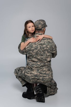 preteen kid hugging serviceman in military uniform during memorial day on grey 