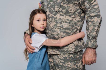 preteen girl hugging brave father in uniform during memorial day isolated on grey 