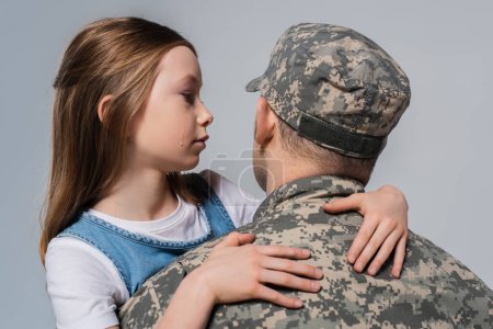 patriotic girl looking at father in army uniform and crying during memorial day isolated on grey