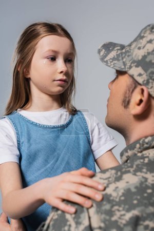 Patriotisches Mädchen sieht Soldat in Armeeuniform an und weint am Gedenktag, isoliert auf grau